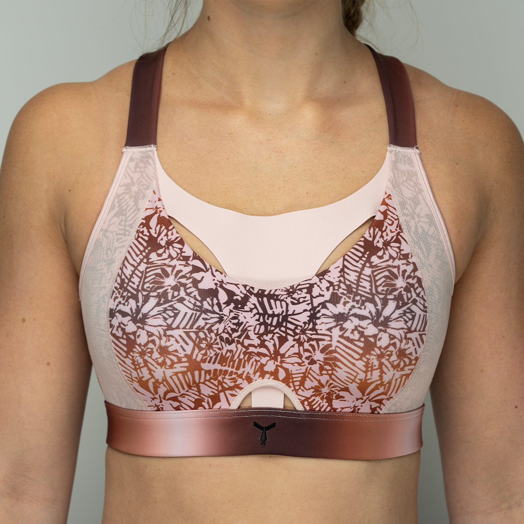 Close-up of the Tigers Eye Orchid sports bra on a model, highlighting the moulded cups, The Vault feature, and the soft baby pink floral pattern on the ombre background for a stylish and supportive fit.